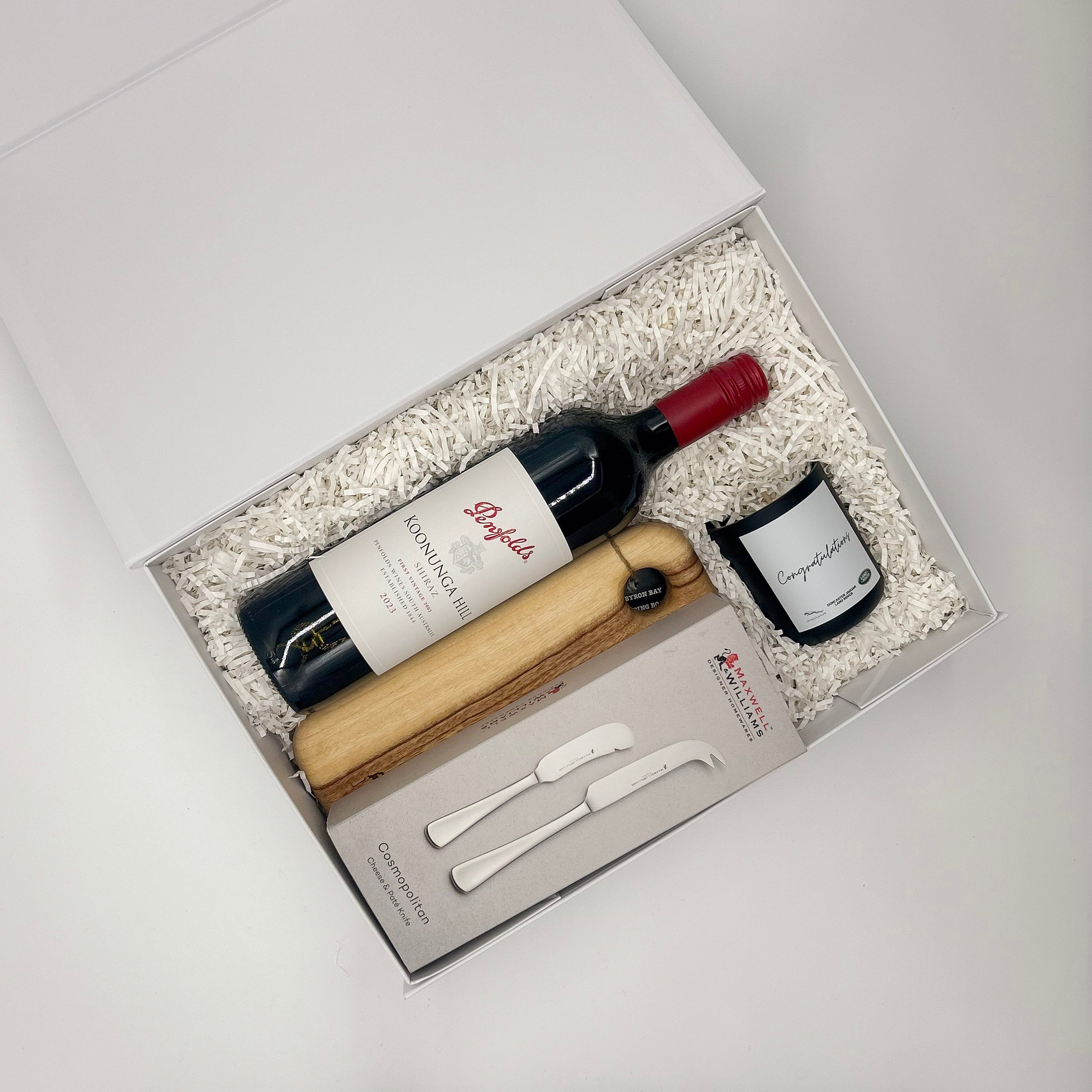 Wine bottle, cheese board, and knives in a gift box on a light gray background